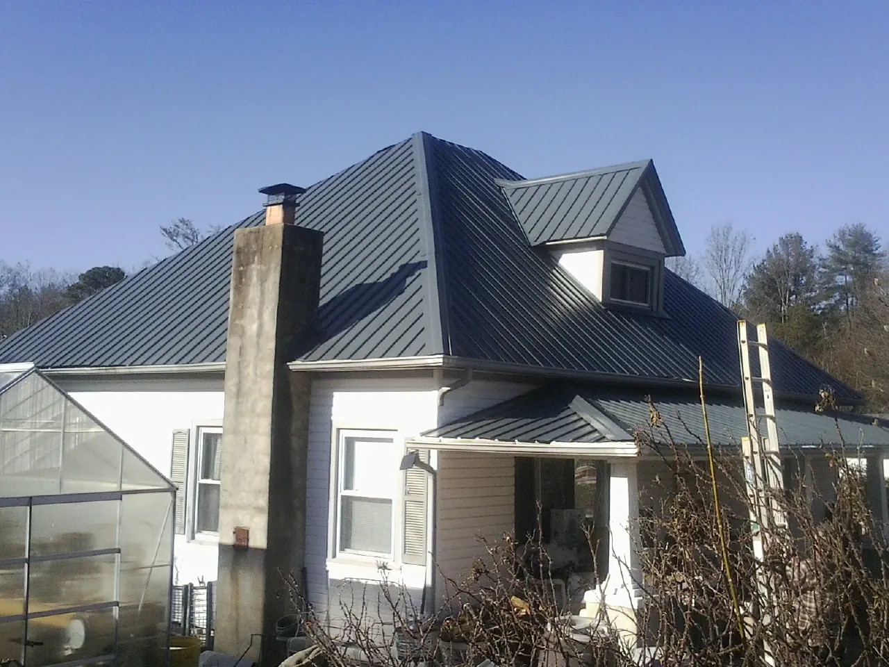 Dark blue standing seam metal roof on a white farmhouse with dormer — Slate & Tile Roof Repair by Roofing Brothers in Coeur d'Alene