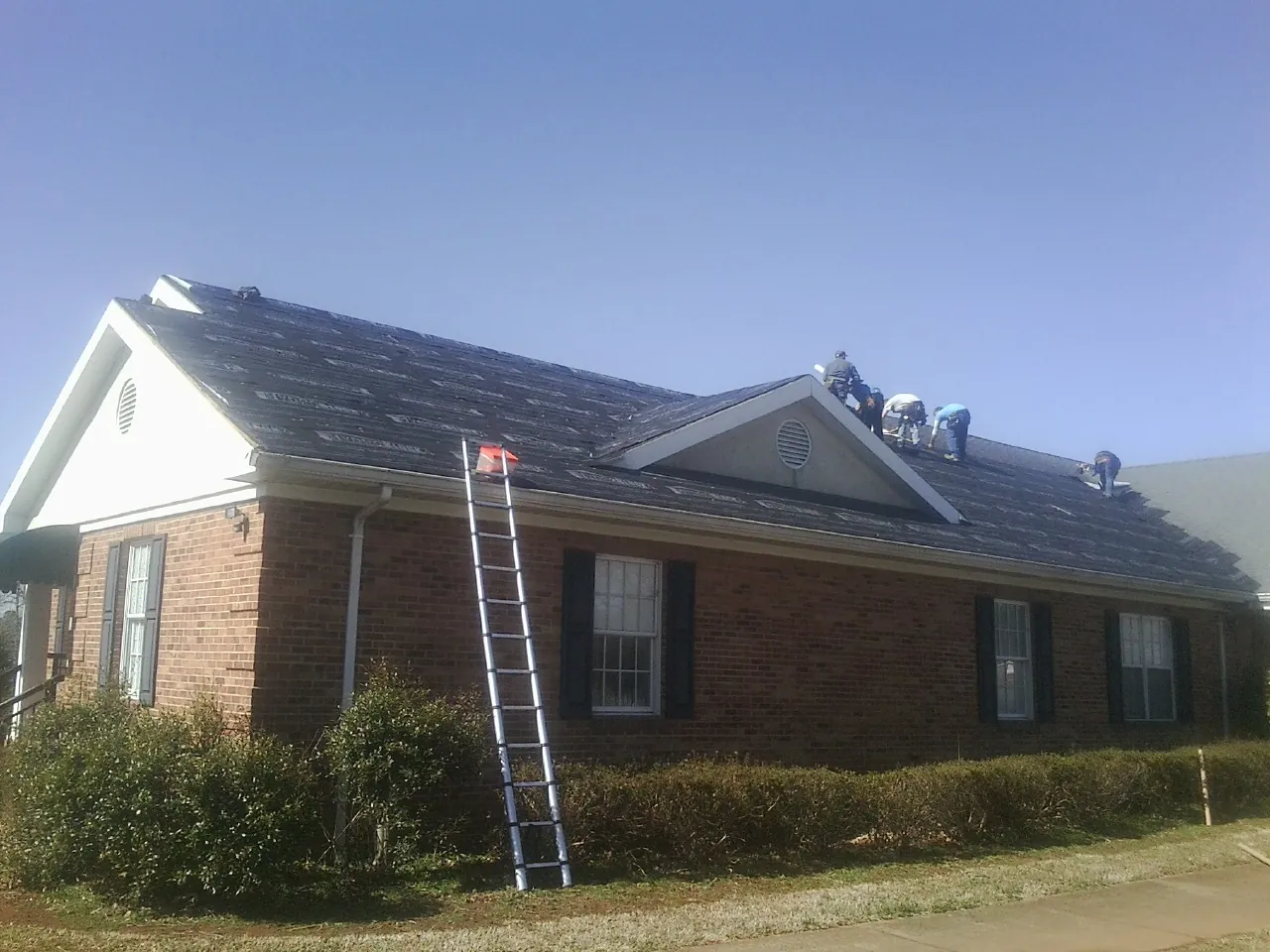 Crew tearing shingles off a brick ranch roof with a ladder set — Emergency Roof Repair work by our crew in Coeur d'Alene