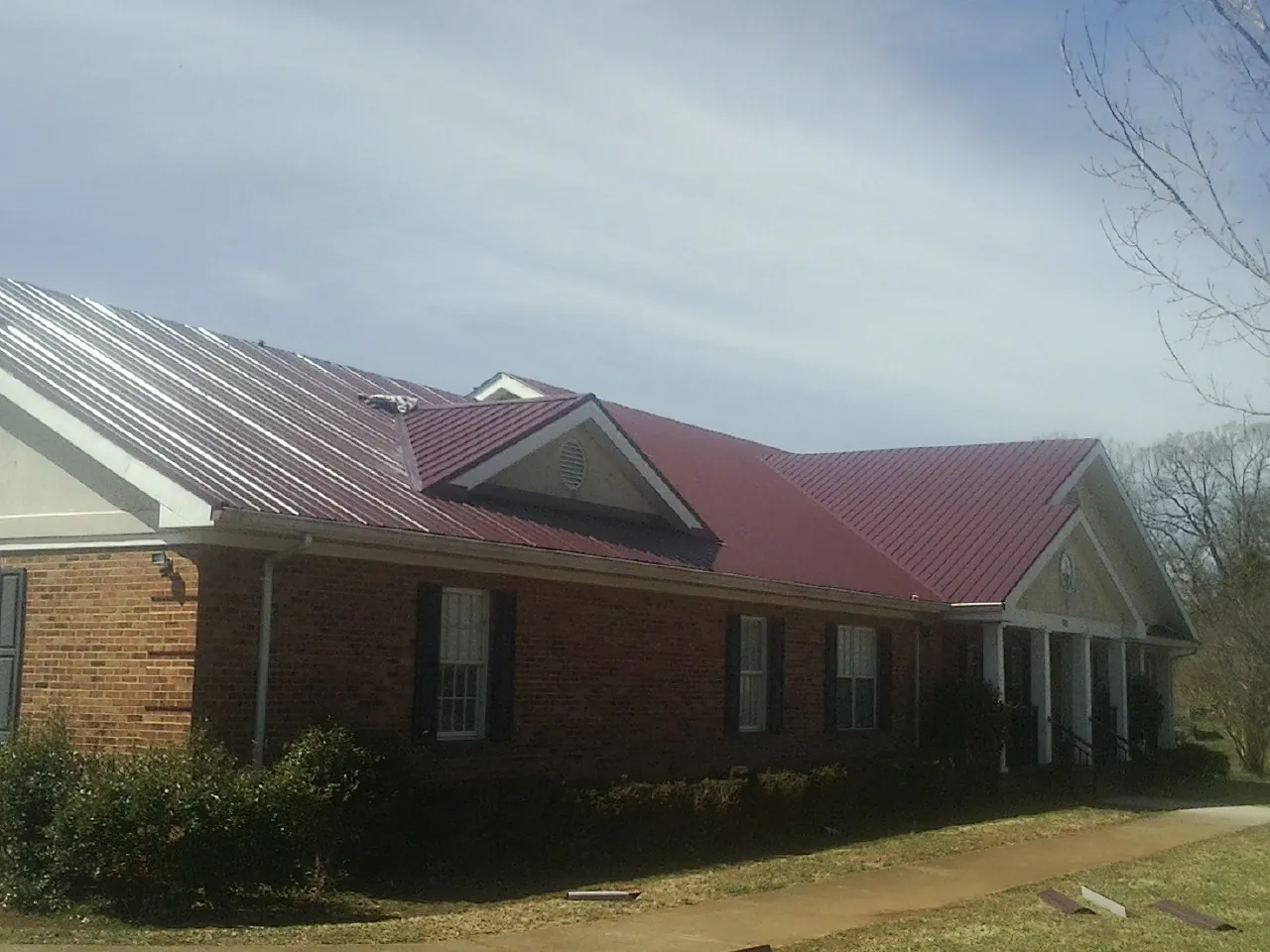Red metal roof with gabled entries on a long brick building, from a Hail Damage Roof Repair job in Coeur d'Alene