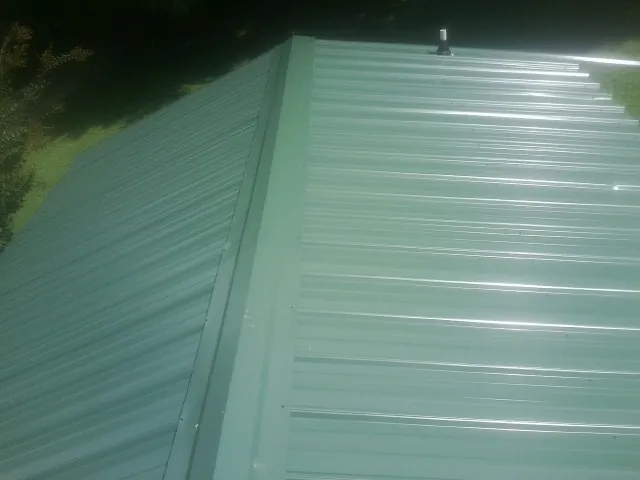 New green metal panels meeting at the ridge of a roof — Flat Roof Repair work by our crew in Coeur d'Alene