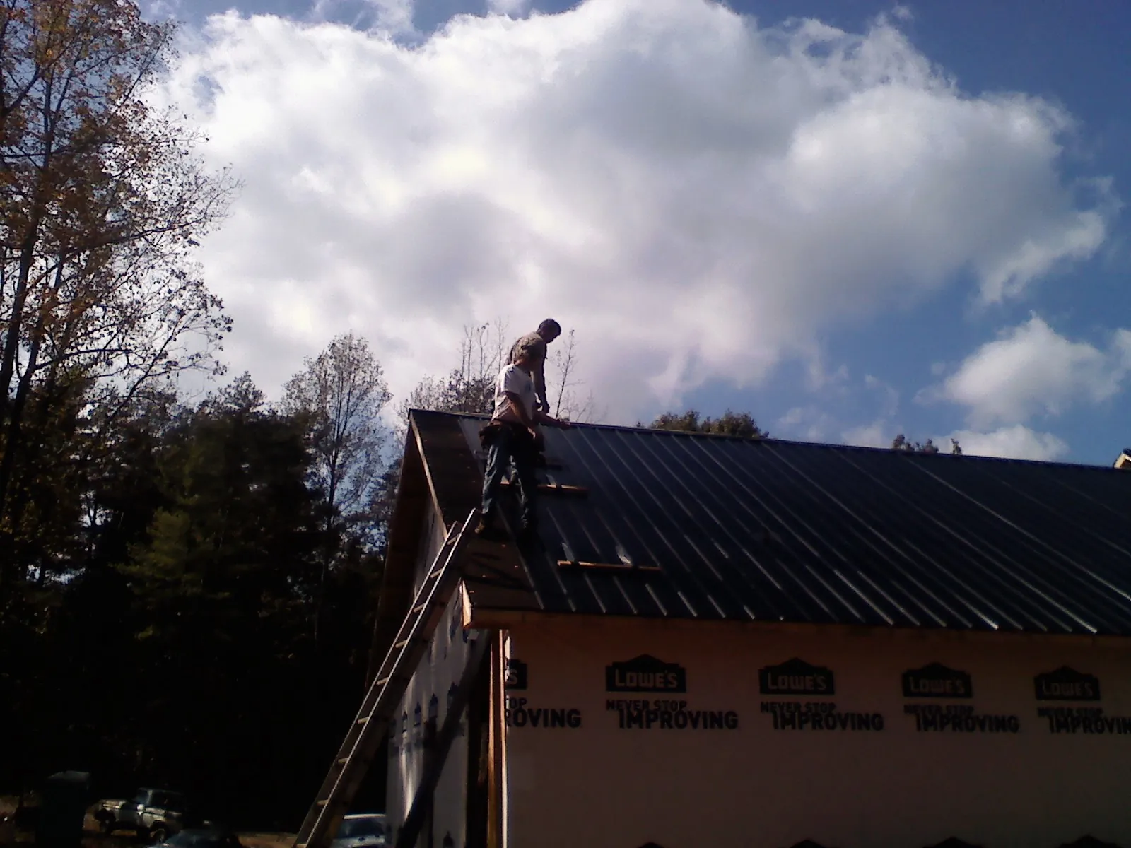 Roofer fastening dark metal panels high against a cloudy sky, from a Roof Inspection job in Coeur d'Alene