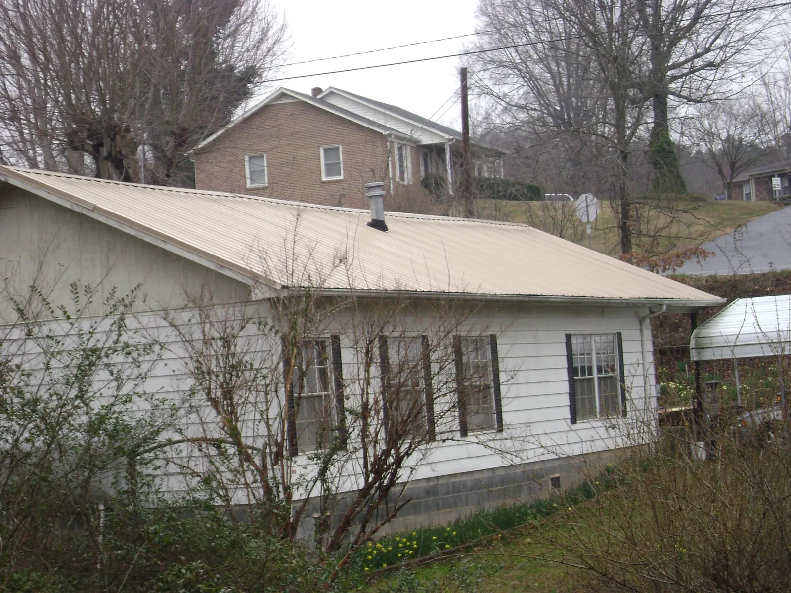 Tan metal roof on a white sided house set into a hillside — Commercial Roofing by Roofing Brothers in Coeur d'Alene